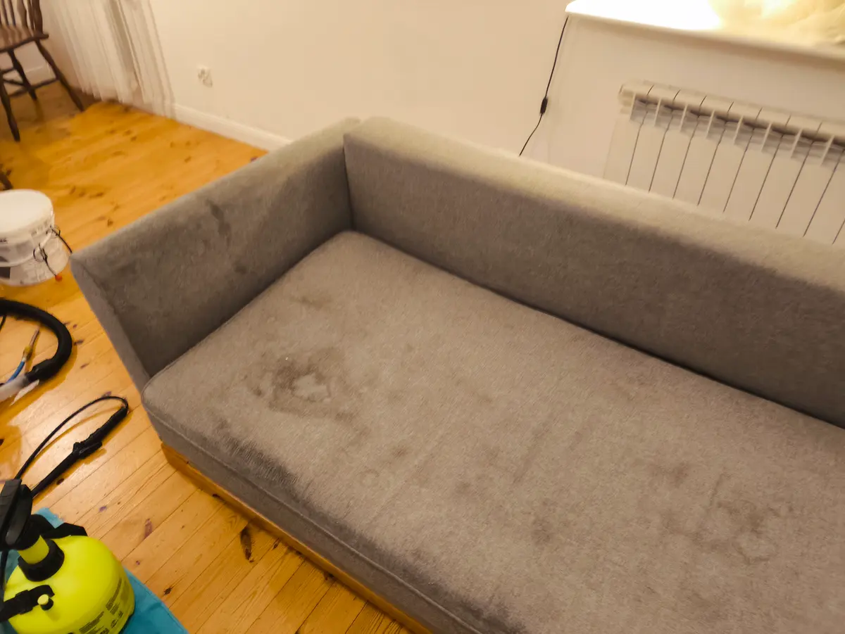 Szara sofa z zaokrąglonymi podłokietnikami przed praniem — ciemne plamy na siedzisku. Pranie kanapy Katowice, SofaGo