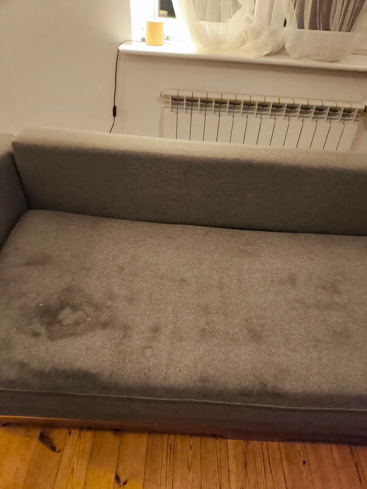 Szara sofa z zaokrąglonymi podłokietnikami przed praniem — ciemne plamy na siedzisku. Pranie kanapy Zabrze, SofaGo